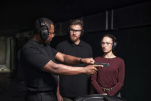 Man demonstrating handling a handgun to two people. All wearing protective earmuffs and safety glasses.